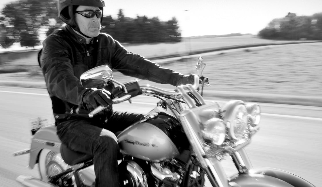 Ken Schmidt wearing a helmet and sunglasses, riding a Harley-Davidson motorcycle